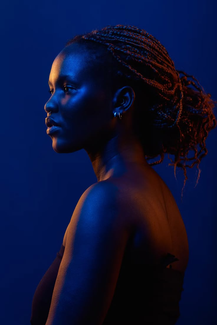 a woman with dreadlocks standing in front of a dark blue background and looking off to the side