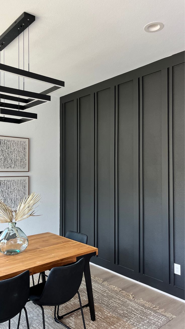 a dining room table with black chairs and art on the wall behind it in front of dark wood paneling