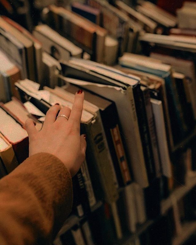 a person reaching for a book in a bookshelf filled with lots of books