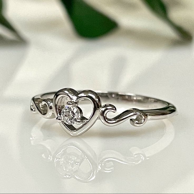 a heart shaped diamond ring sitting on top of a white table next to some flowers