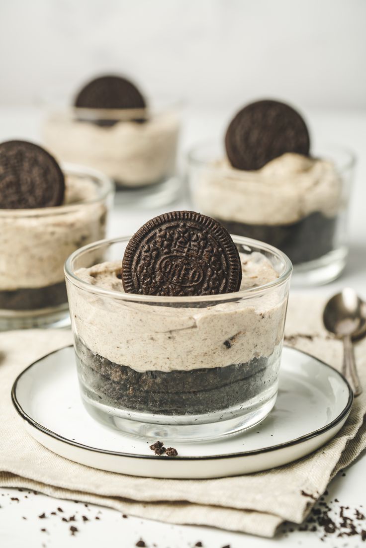 three desserts with oreo cookies and cream in glass dishes on a white table