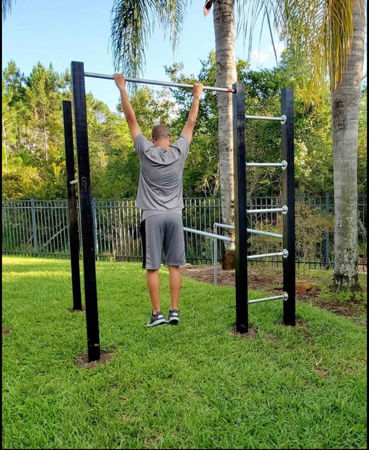 a man is doing pull ups in the grass with palm trees behind him and his hands on the bars