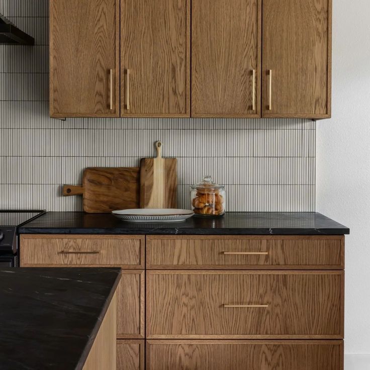 a kitchen with wooden cabinets and black counter tops in front of a white tiled wall