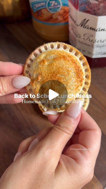 a person holding a small pie on top of a wooden table with condiments in the background