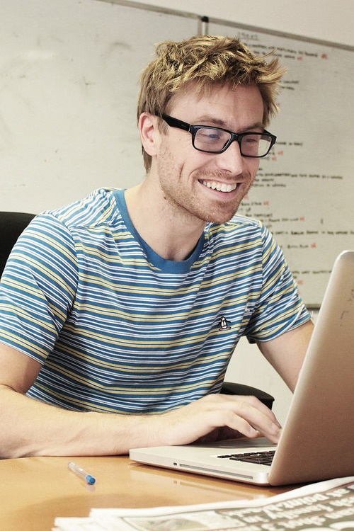 a man sitting at a desk with a laptop computer in front of him and smiling