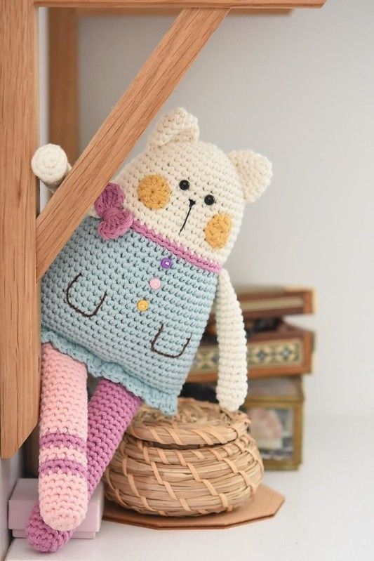 a crocheted teddy bear sitting on top of a basket next to a wooden shelf