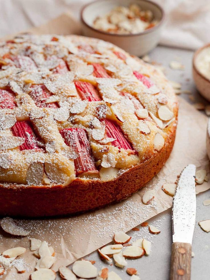 a cake covered in powdered sugar and topped with sliced rhubarb slices