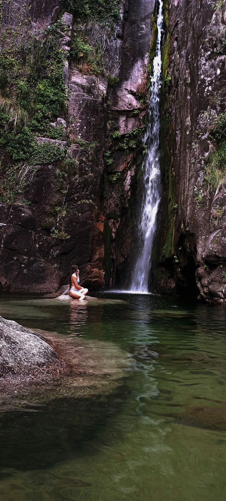 a person sitting in the water next to a waterfall