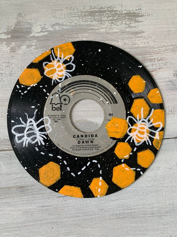 an orange and black disk with bees on it sitting on a white wooden table next to a wall