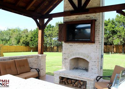 an outdoor living area with couches and a television on the brick fireplace in the center