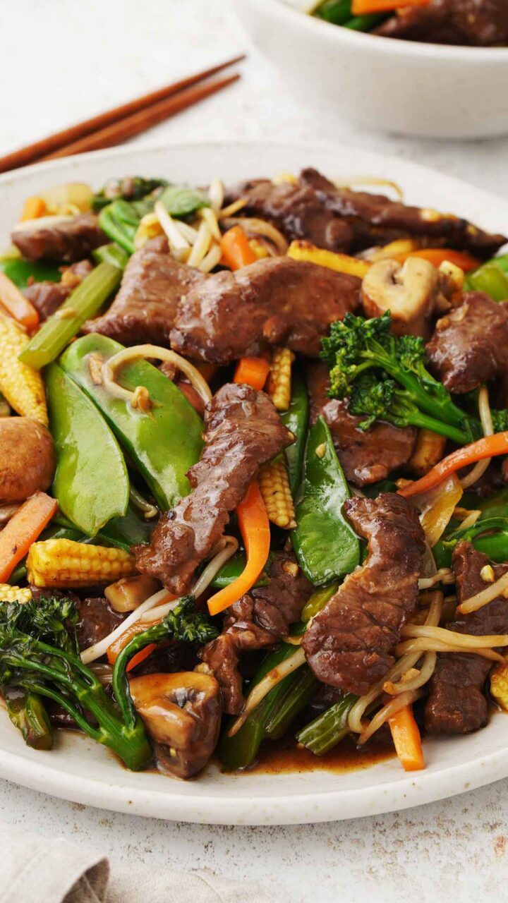 beef and vegetable stir fry on a plate with chopsticks next to the bowl