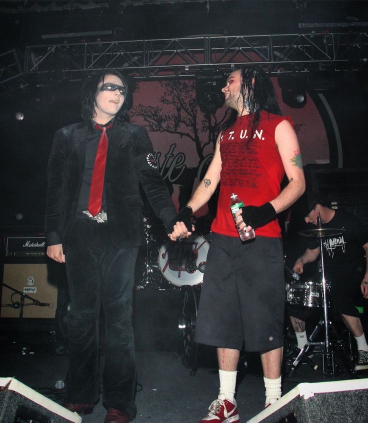 two men dressed in black and red are standing on stage with one holding the other's hand