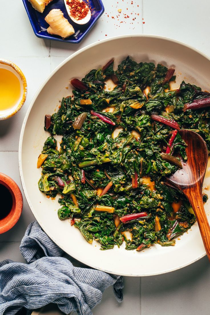 a white bowl filled with greens next to two cups of tea