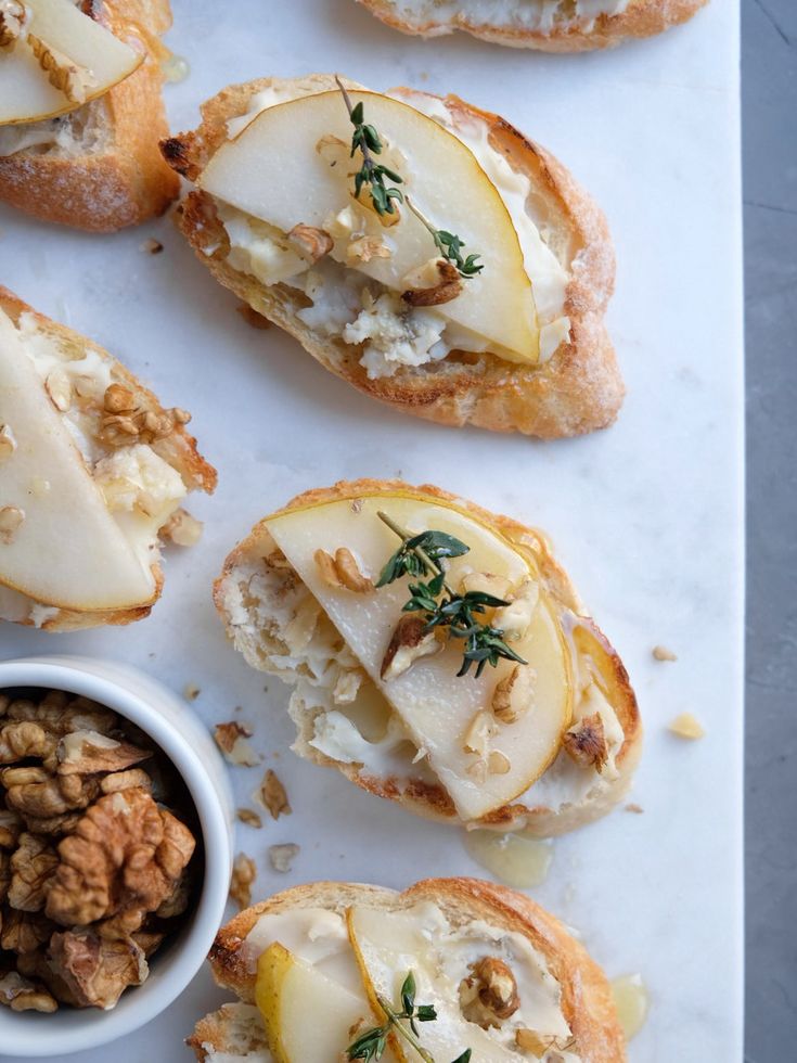 several pieces of bread with pears and walnuts on them next to a small bowl of nuts