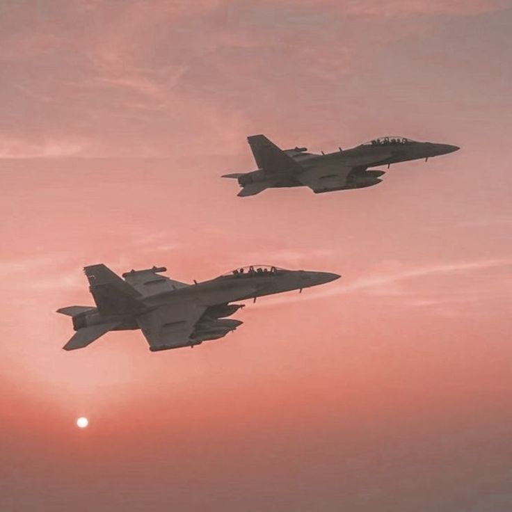 two fighter jets flying in the sky at sunset