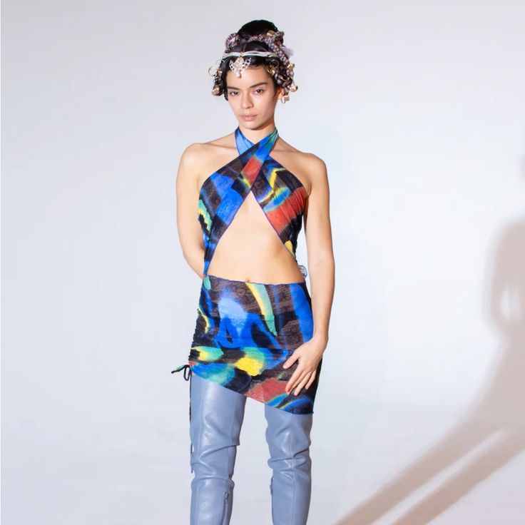 a woman is standing in front of a white wall wearing a colorful top and pants