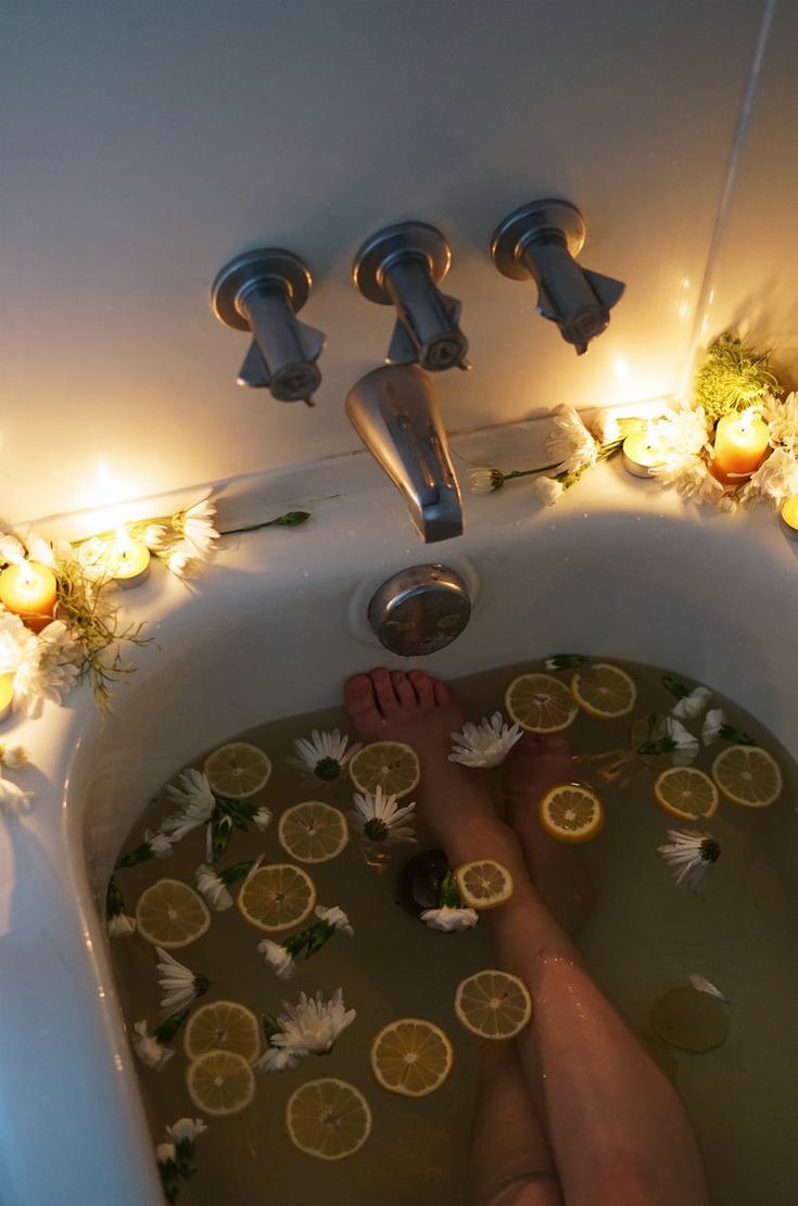 a person in a bathtub filled with water and lemons next to candles on the wall