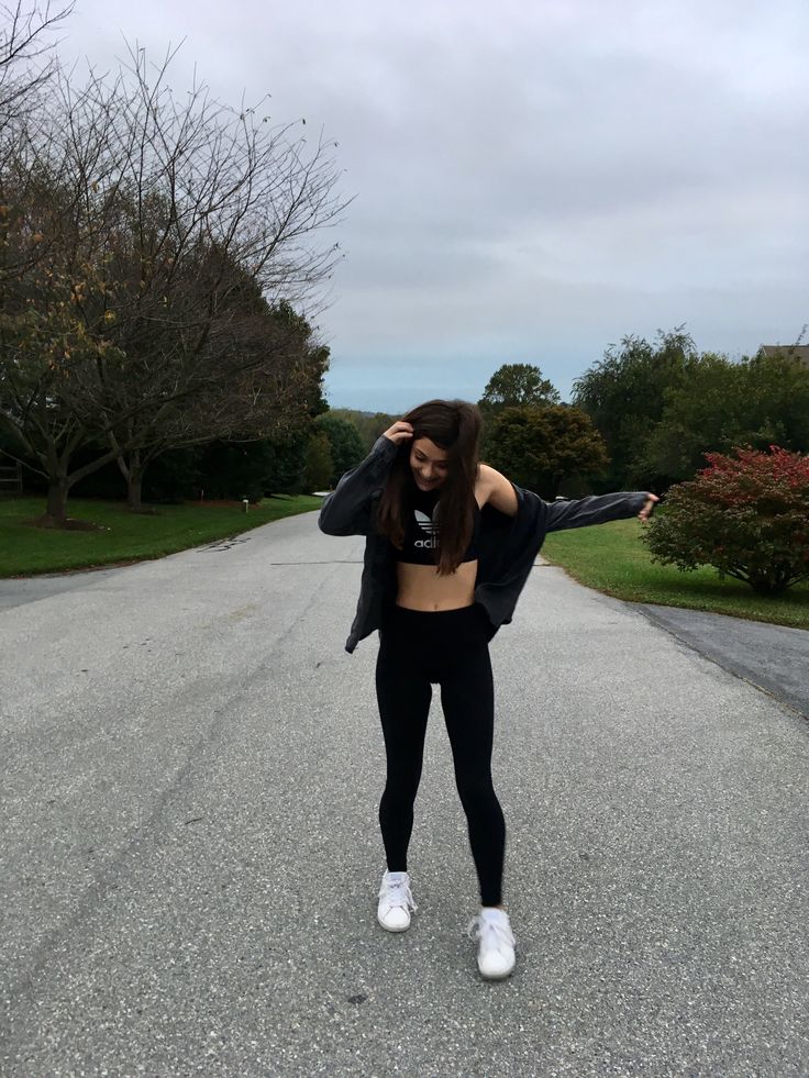 a woman standing in the middle of an empty road with her arms out and hands behind her head