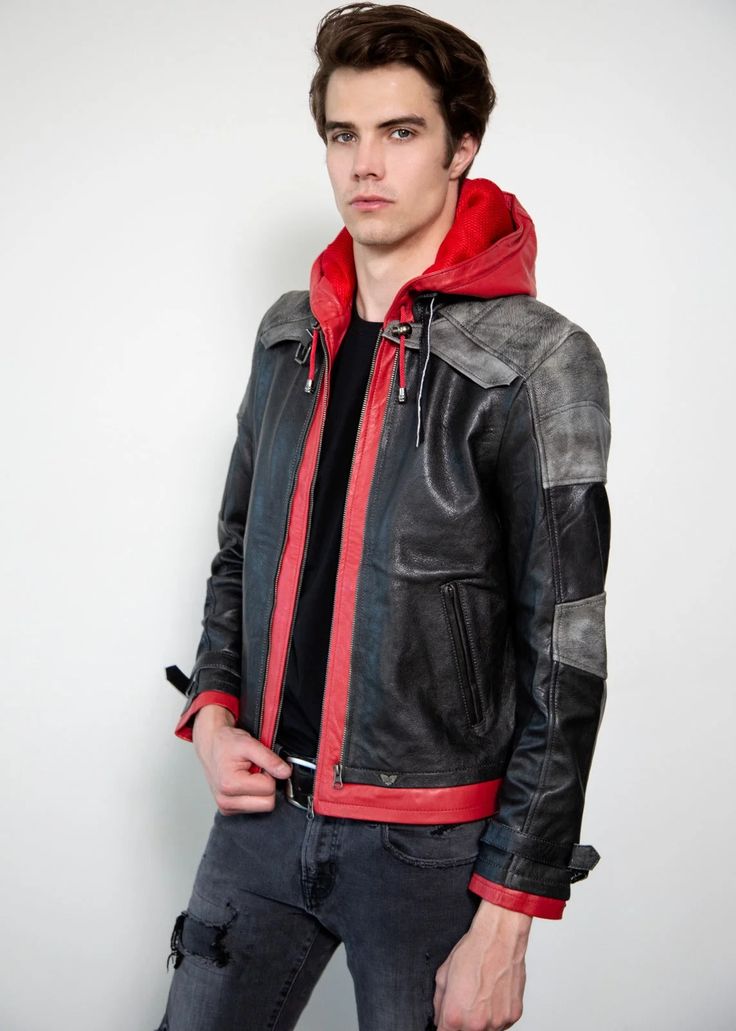 a young man wearing a leather jacket and red hoodie standing in front of a white wall