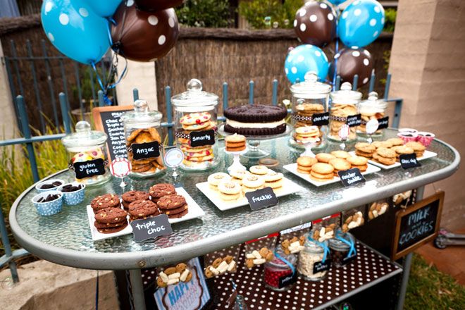 a table topped with lots of desserts next to blue and brown balloons in the air