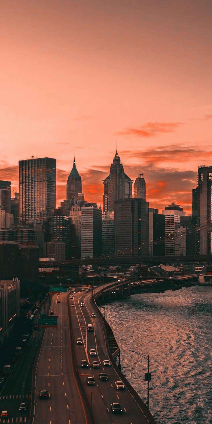 the city skyline is lit up at sunset with cars driving on the road in front of it