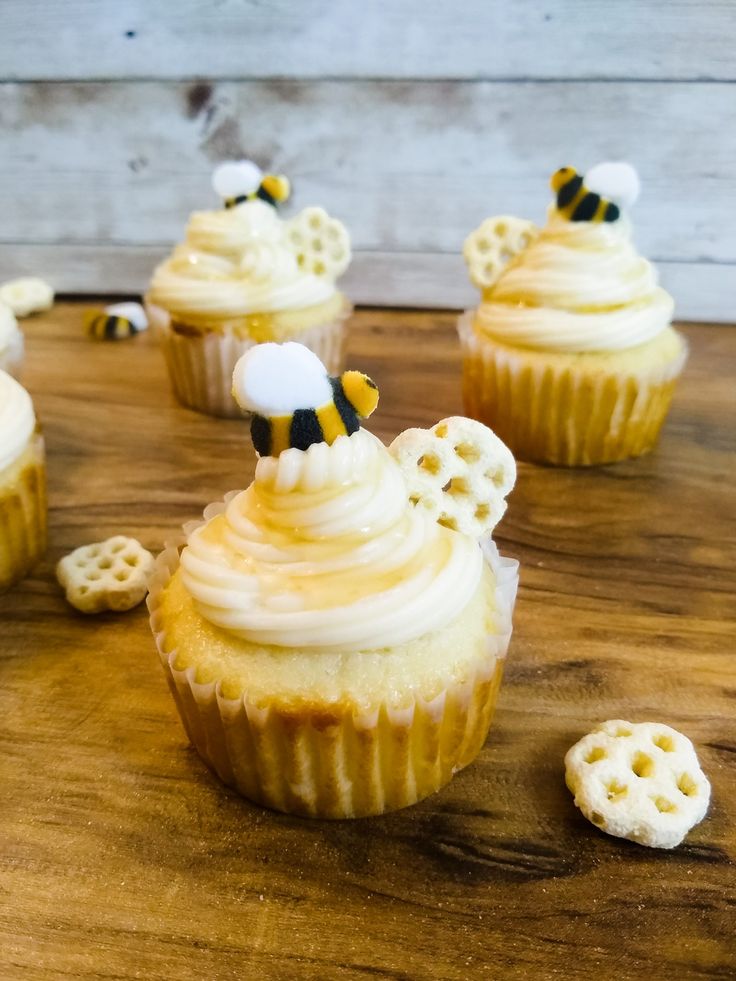 some cupcakes with white frosting and bees on them sitting on a table