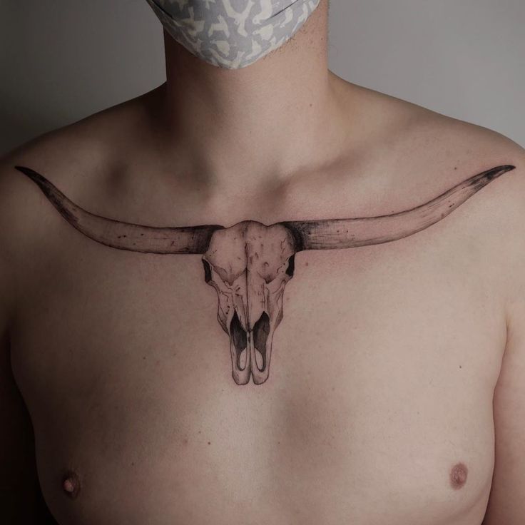 a man with a mask on his face has a bull's skull tattooed on his chest