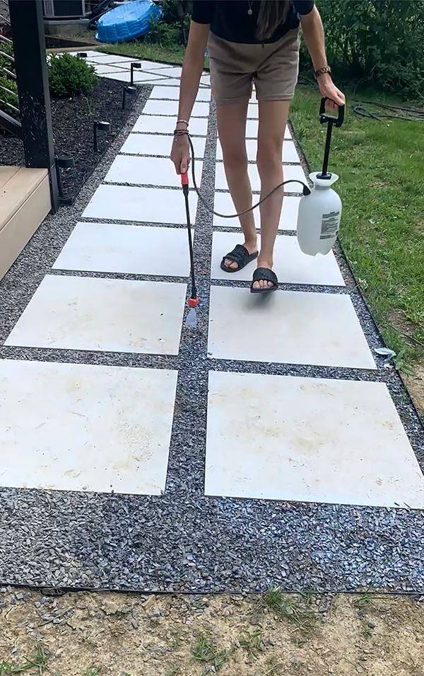 a woman is using a sprayer to paint the walkway