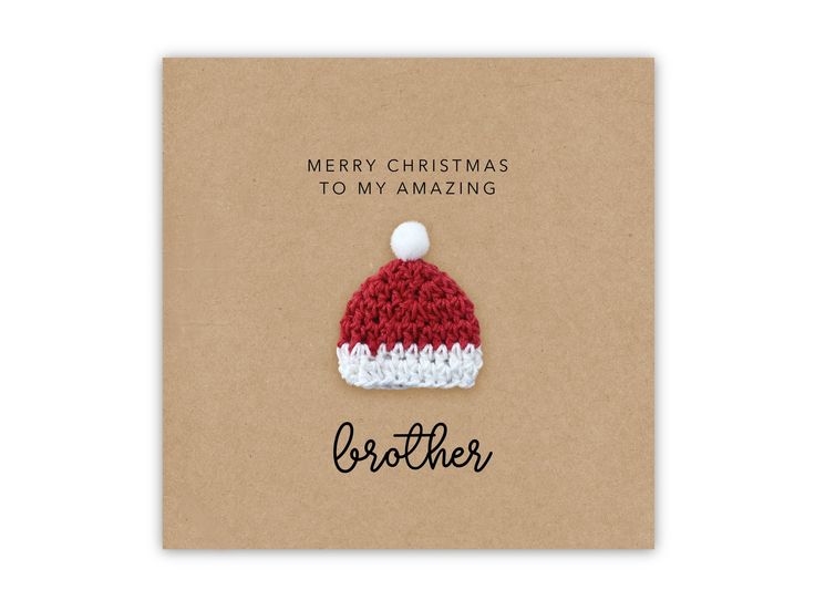 a red and white knitted christmas hat on top of a brown card that says merry christmas