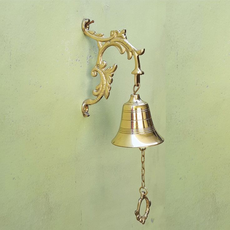 a golden bell hanging from the side of a green wall