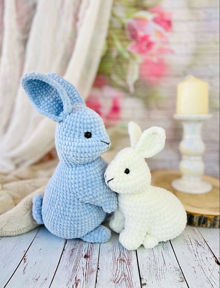 two crocheted stuffed animals sitting next to each other on a wooden table with flowers in the background