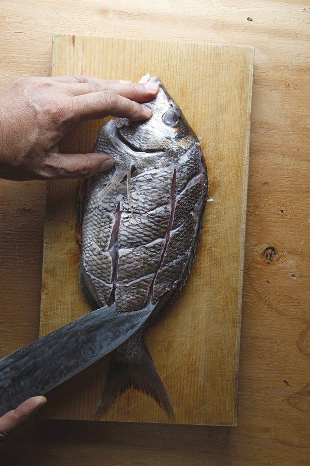 a person cutting up a fish on top of a wooden table next to a knife