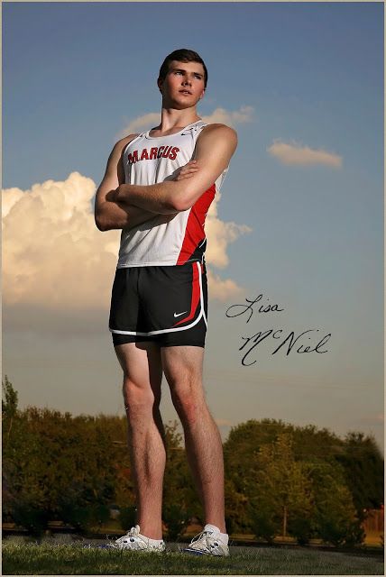 a man standing in the grass with his arms crossed, wearing shorts and a tank top