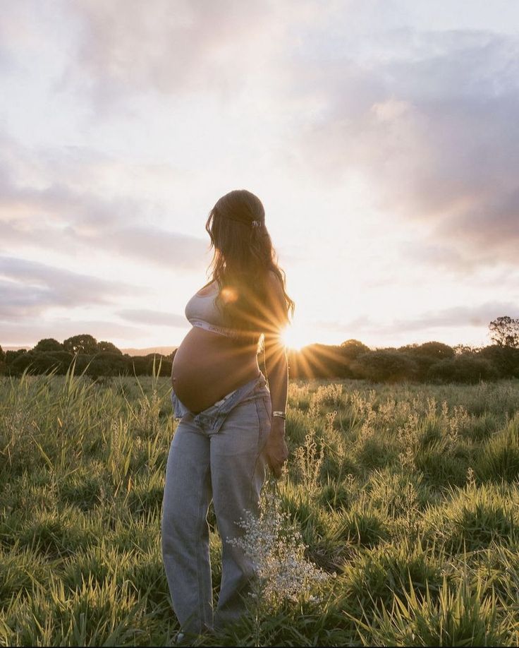 a pregnant woman standing in a field with the sun shining down on her belly and back