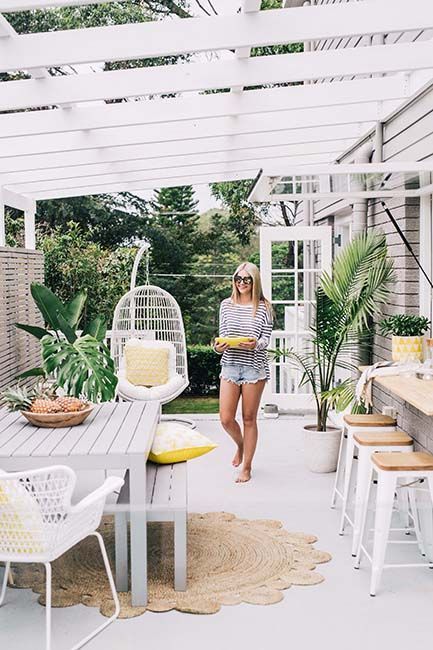 a woman standing in the middle of an outdoor patio with white furniture and yellow cushions