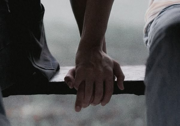 two people sitting on a bench with their hands touching each other's fingertipss