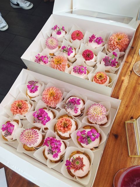 there are many cupcakes with flowers in the box on the table next to each other