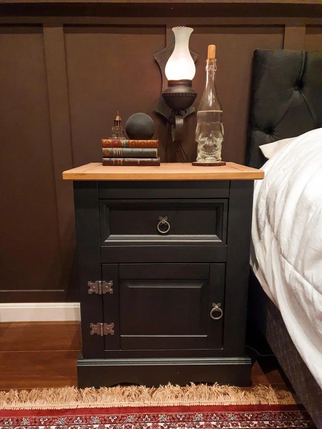 a night stand next to a bed with a bottle and lamp on top of it