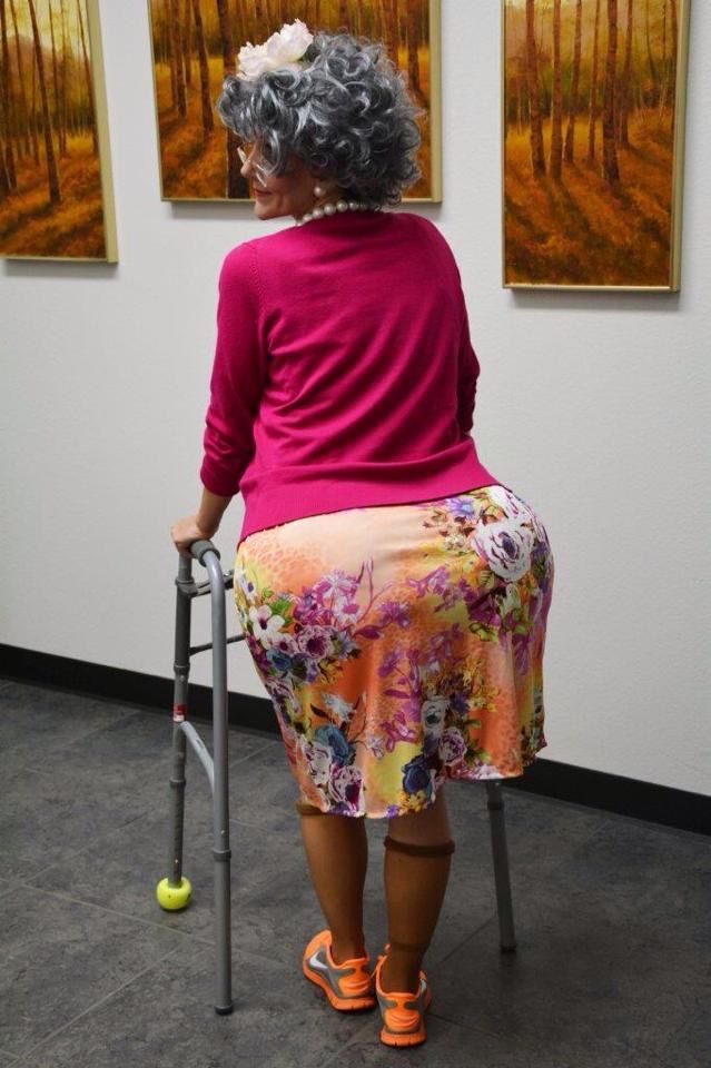 an older woman sitting on a chair with a walker in front of her and two paintings behind her