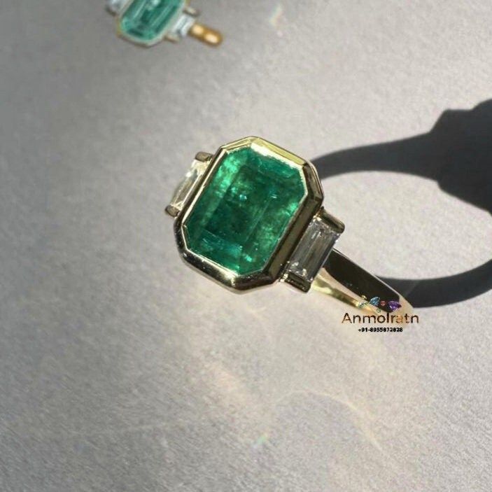 an emerald and diamond ring is shown on a table