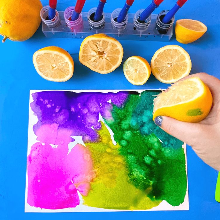 someone is painting some lemons and oranges with watercolor on the paper next to them