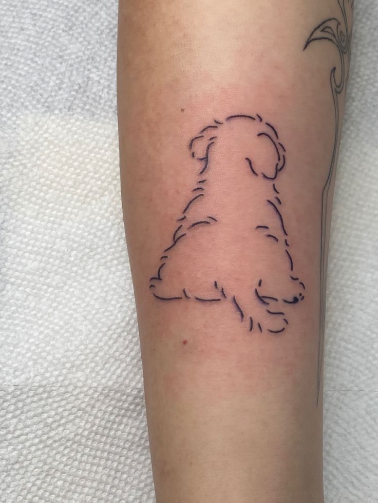 a small dog tattoo on the left forearm and leg, with a flower in its mouth