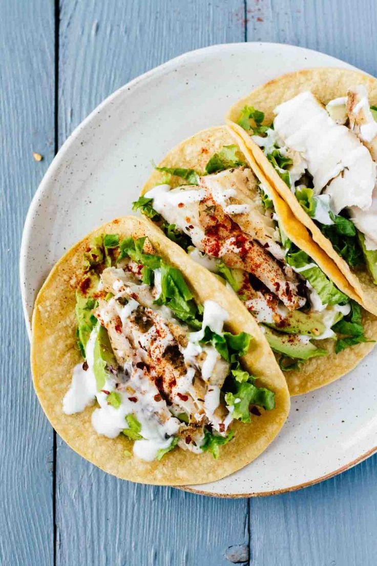 two fish tacos with lettuce and sour cream sauce on a white plate