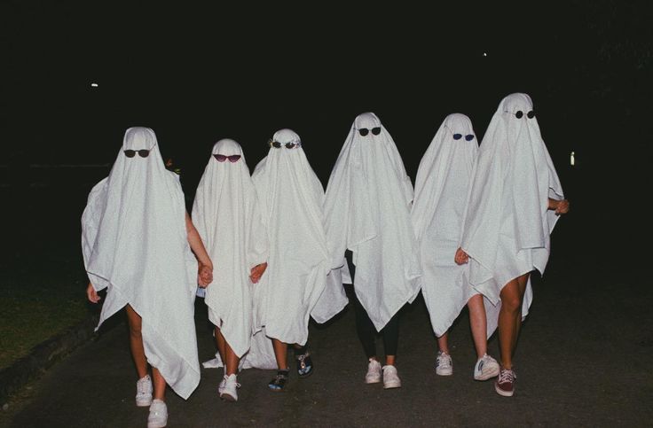 four people in white ghost costumes walking down the street at night with their hands on their hips