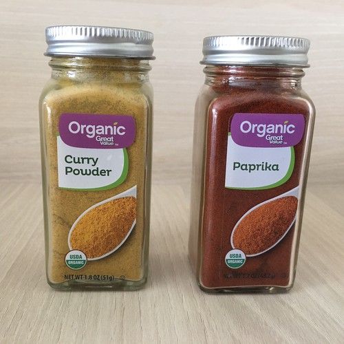 two jars filled with spices sitting on top of a wooden table next to each other