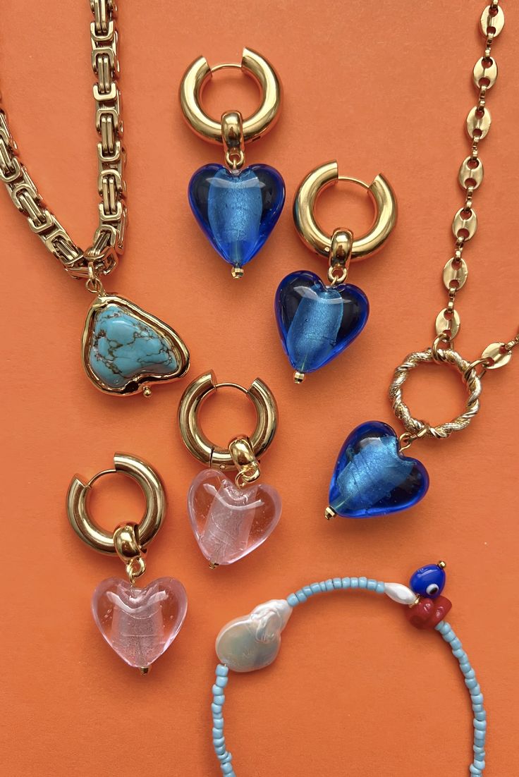 This show-stopper charm necklace will have you seeing hearts! Layer it with the Mati Mati Necklace in Blue for a fun stack. 24K Gold plated brass chain and circle with a Murano glass heart pendant. Length: 15.75 inches Handmade in Greece. Trendy Glass Jewelry With Lobster Clasp, Trendy Glass Jewelry As A Gift, Blue Heart Charm Necklaces, Trendy Round Jewelry With Heart Charm, Trendy Gold Jewelry With Heart Beads, Trendy Round Glass Jewelry, Trendy Blue Glass Necklace, Blue Heart Charm Necklace, Trendy Blue Glass Jewelry