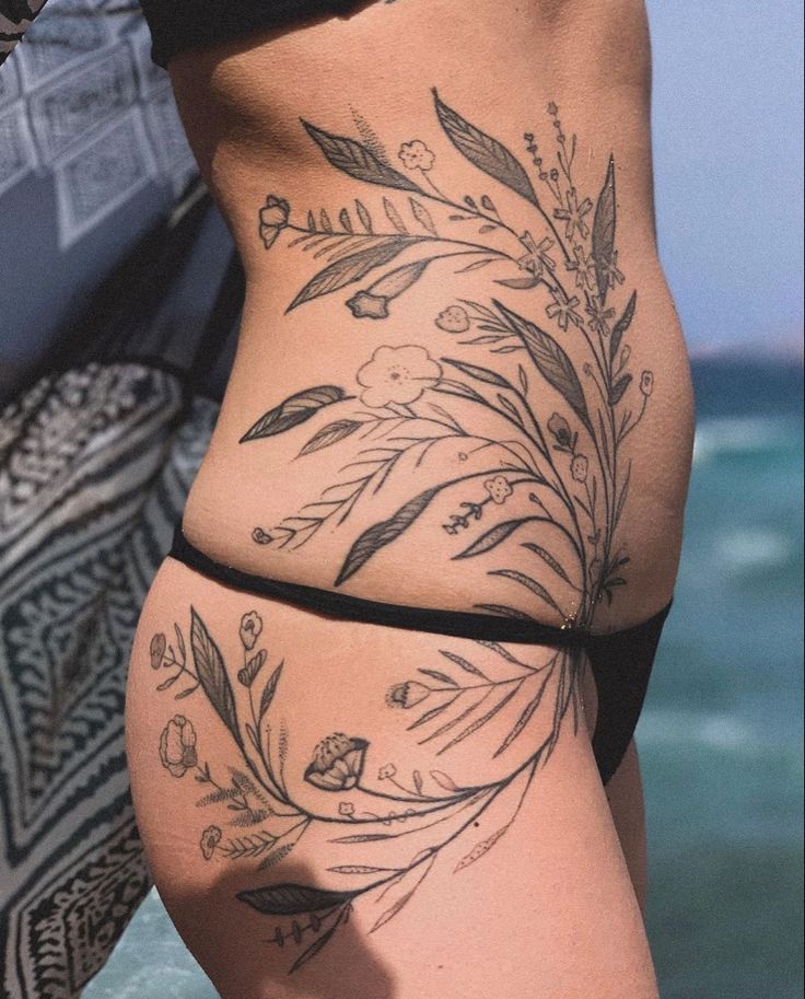 a woman's lower body with tattoos on her legs and the ocean in the background