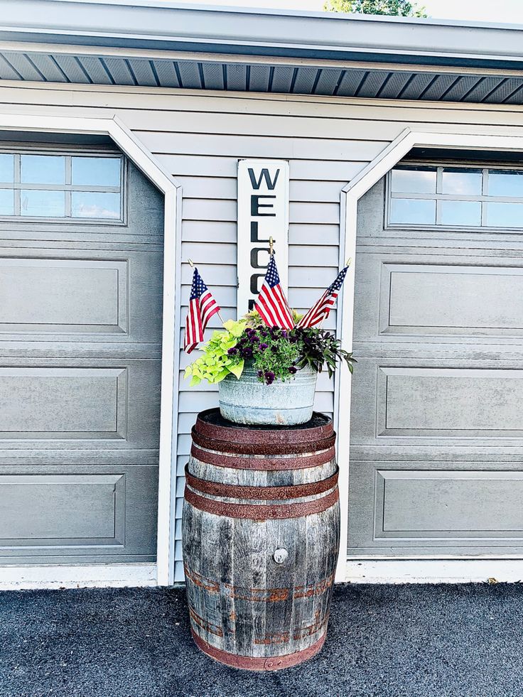 a wooden barrel with flowers and an american flag on it in front of two garage doors