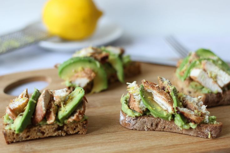 several pieces of bread with avocado and chicken on them sitting on a cutting board