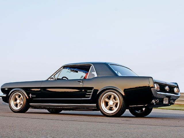 an old black muscle car driving down the road